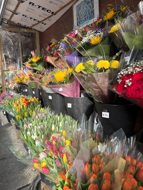 A display of fresh flower bouquets arranged in black buckets inside a flower shop, featuring a variety of vibrant blooms such as yellow chrysanthemums, pink and orange tulips, purple irises, and red r