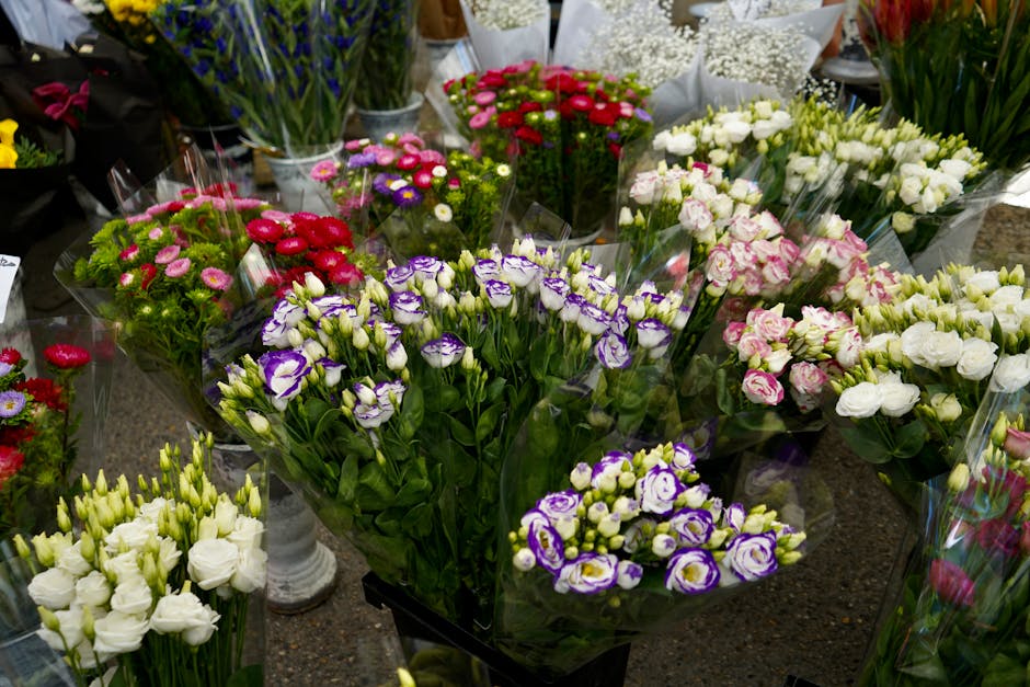 A variety of fresh flower bouquets displayed on a table in a floral shop, featuring tightly packed arrangements of flowers like white, purple, pink, and red blooms, all wrapped in clear plastic sheets