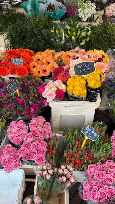A vibrant display of fresh flower bouquets arranged on a market table, featuring a variety of blooms including bright orange gerbera daisies, soft pink roses, yellow chrysanthemums, and red tulips, ea