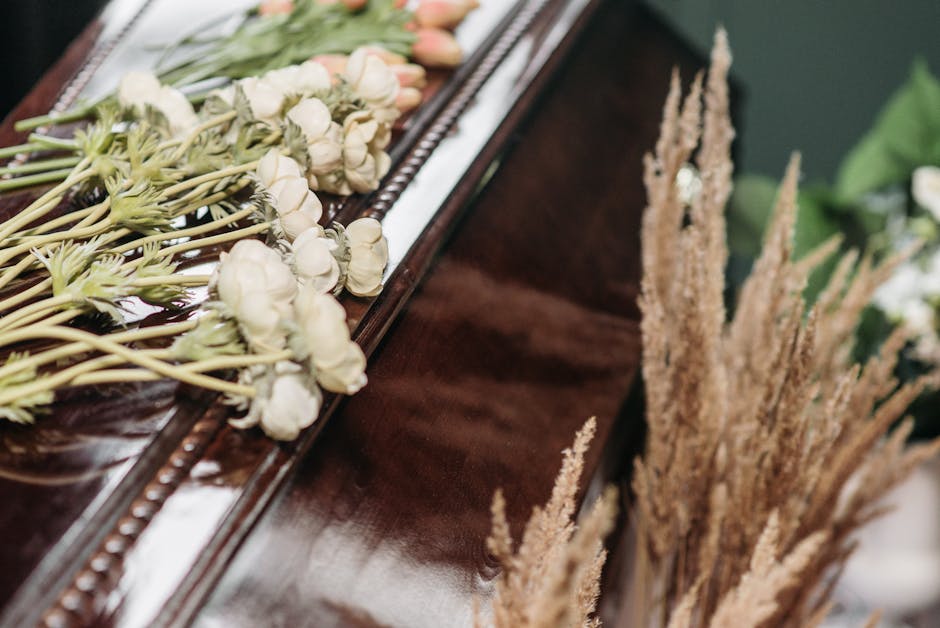 Close-up of a floral arrangement placed on a polished dark wooden surface, featuring delicate white flowers with tightly packed petals, arranged in a linear fashion along the edge. The flowers are fre